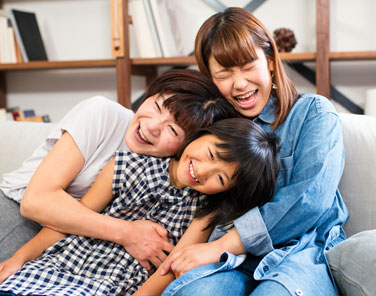 Grandmother, mother and daughter laughing and hugging on a sofa