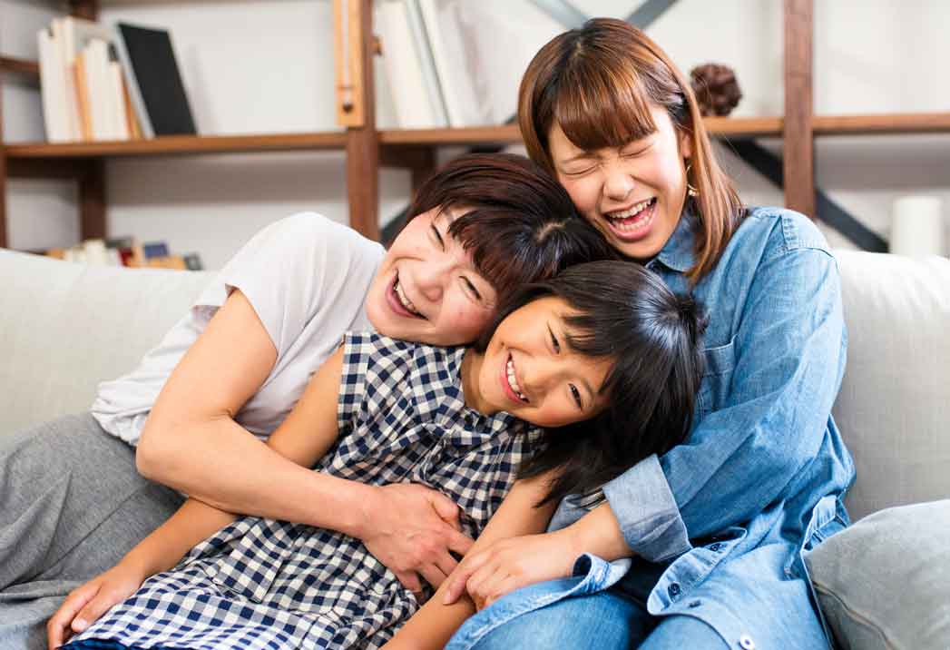 Grandmother, mother and daughter laughing and hugging on a sofa